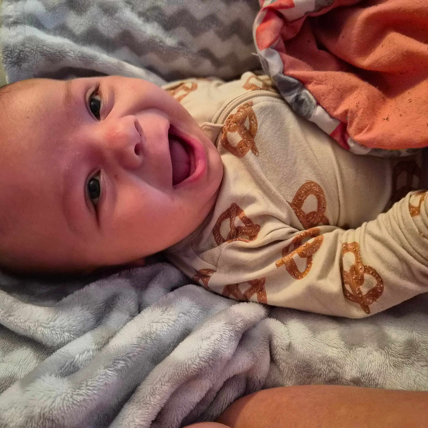 Elijah joined the competition — help win amazing prizes! baby, bed, blanket, child, comfort, cozy, cute, face, hand, happy, head, infant, lying_down, onesie, portrait, pretzel_pattern, skin, sleepwear, smiling, soft_texture