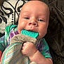 baby, infant, teething_toy, tie_dye_clothing, hand, face, blue_eyes, blanket, patterned_blanket, quilted_blanket, cute, close_up, child, young_child, soft_skin, indoor, person, lying_down, colorful_clothing, exploration