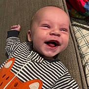 Jace is registered to the contest to win money with this photo: baby, infant, smiling, striped_clothing, onesie, orange_fox, couch, blanket, happy, face, head, lying_down, child, indoor, expression, person, cute, young, comfortable, portrait