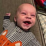 baby, infant, smiling, striped_clothing, onesie, orange_fox, couch, blanket, happy, face, head, lying_down, child, indoor, expression, person, cute, young, comfortable, portrait