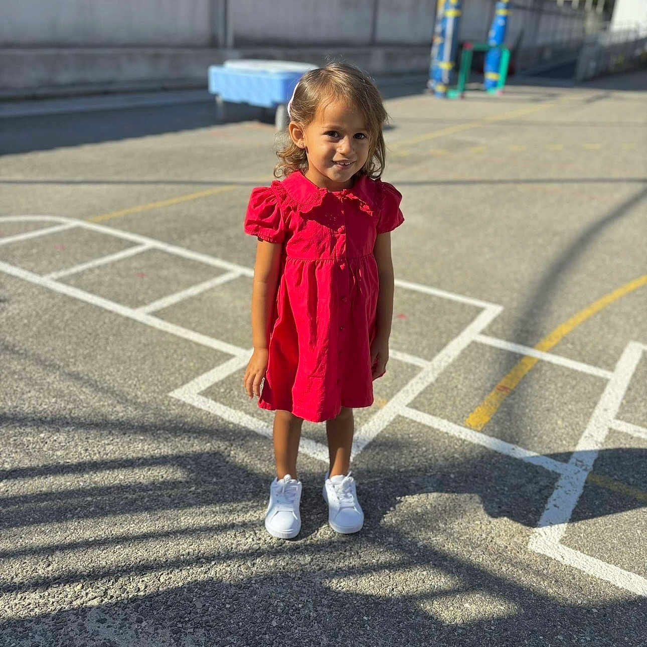 Inaya a rejoint le concours — aidez-le/la à gagner de superbes lots ! casual, child, concrete, curly_hair, daytime, fence, girl, happy, hopscotch, outdoor, person, playground, playing, recess, red_dress, shadow, smile, sunlight, white_shoes, young