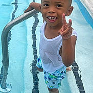 Aayden is registered to the contest to win money with this photo: child, boy, swimming_pool, water, tank_top, swim_trunks, smiling, peace_sign, summer, outdoor, metal_railing, barefoot, happy, young, playful, casual_clothing, recreation, fun, light, daylight