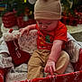 baby, beige_pants, blanket, child, christmas, cozy, cute, decorations, festive, gift_box, holiday, indoor, knit_hat, present, red_bow, red_shirt, reindeer_ears, sitting, stocking, toy