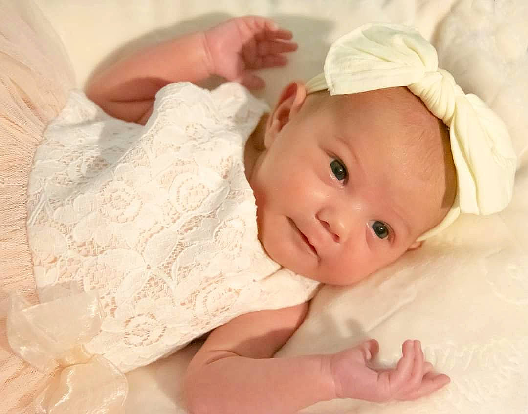 Charity is registered to the contest to win money with this photo: baby, baby_products, baby_toddler_clothing, bonnet, cheek, child, costume_accessory, day_dress, embellishment, hair_accessory, headband, headgear, linens, lip, mouth, nose, peach, person, portrait_photography, skin