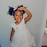 Bethlehem is registered to the contest to win money with this photo: child, girl, toddler, portrait, smiling, happy, indoors, white_dress, formalwear, curly_hair, hair_bows, standing, salute, shoes, wood_floor, wall, doorway, jewelry, fashion, celebration