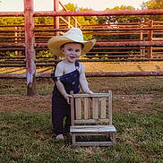 Alexander joined the competition — help win amazing prizes! toddler, child, cowboy_hat, overalls, barefoot, grass, wooden_chair, fence, outdoor, sunset, nature, rustic, playful, smiling, portrait, young_child, rural, farm, greenery, sunlight