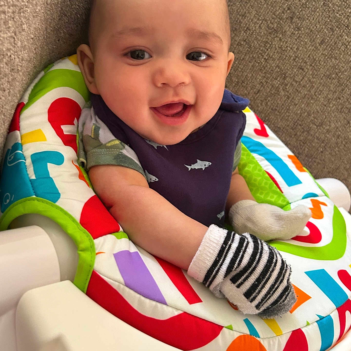 Kiante is registered to the contest to win money with this photo: baby, bib, cheerful, closeup, clothing, colorful, cute, expression, face, happy, head, high_chair, indoor, infant, mittens, pattern, person, seated, smiling, striped
