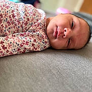 Leila is registered to the contest to win money with this photo: baby, newborn, swaddle, floral_pattern, sleepy, face, infant, lying_down, soft_surface, portrait, closeup, child, person, indoor, blurred_background, peaceful, resting, cute, skin, head