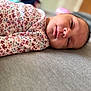 baby, newborn, swaddle, floral_pattern, sleepy, face, infant, lying_down, soft_surface, portrait, closeup, child, person, indoor, blurred_background, peaceful, resting, cute, skin, head