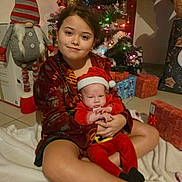 Elio a rejoint le concours — aidez-le/la à gagner de superbes lots ! child, baby, christmas_tree, presents, ornaments, santa_hat, holiday, festive, sibling, sitting, blanket, indoors, cozy, portrait, gift_wrap, toys, smile, living_room, gifts, seasonal_decor