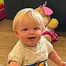 baby, blonde_hair, blue_eyes, casual_clothing, child, childhood, cute, floor, happy, indoor, person, playful, plush_toy, short_sleeves, sitting, smiling, toddler, toy, tshirt, wooden_floor