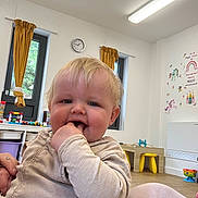 Jaxon joined the competition — help win amazing prizes! baby, child, blonde_hair, indoor, toys, curtains, windows, clock, wall_decor, unicorn, rainbow, table, chair, floor, happy, smiling, person, casual_clothing, hand_in_mouth, playroom