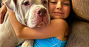 Bodhi joined the competition — help win amazing prizes! child, dog, hugging, couch, blanket, indoor, smiling, white_dog, blue_tank_top, brown_couch, comfort, pet, friendship, relaxation, home, happy, closeup, face, arm, casual_clothing