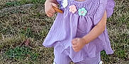 Elena participe au concours pour gagner de l'argent avec cette photo : toddler, child, grass, sidewalk, outdoor, purple_clothing, flower_decorations, sandals, holding_biscuit, walking, young_child, curious_expression, short_hair, summer, daylight, nature, casual, cute, person, small