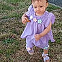 toddler, child, grass, sidewalk, outdoor, purple_clothing, flower_decorations, sandals, holding_biscuit, walking, young_child, curious_expression, short_hair, summer, daylight, nature, casual, cute, person, small