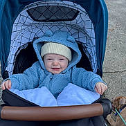 Ashton joined the competition — help win amazing prizes! baby, child, stroller, blue_hoodie, hat, smiling, outdoor, dog, leash, pavement, happy, cute, warm_clothing, infant, person, pet, canine, blanket, hood, daylight