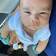 Ethan joined the competition — help win amazing prizes! baby, child, infant, person, car_interior, seat, hand, wristband, clothing, socks, footwear, steering_wheel, floor_mat, adult_hand, blue_clothing, closeup, portrait, serious_expression, indoor, skin
