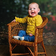 Hanaé participe au concours pour gagner de l'argent avec cette photo : baby, child, smiling, wicker_chair, yellow_shirt, blue_pants, socks, indoor, portrait, happy, cute, seated, wooden_floor, rosy_cheeks, blue_eyes, natural_light, cozy, warm_colors, infant, candid