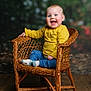 baby, child, smiling, wicker_chair, yellow_shirt, blue_pants, socks, indoor, portrait, happy, cute, seated, wooden_floor, rosy_cheeks, blue_eyes, natural_light, cozy, warm_colors, infant, candid