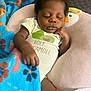 Rayquan is registered to the contest to win money with this photo: baby, sleeping, blanket, blue, floral, onesie, text_on_clothing, pillow, duck_shape, infant, peaceful, curly_hair, indoor, resting, child, cute, soft_texture, hand, face, cozy