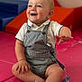 baby, child, smiling, sitting, overalls, white_shirt, play_mat, indoor, happy, cute, infant, person, face, hand, foot, toy, pacifier, striped_clothing, play_area, soft_surface