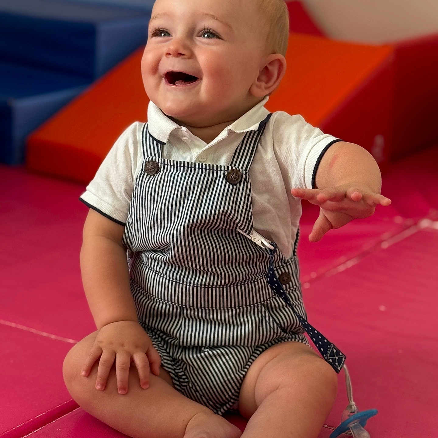 Giulian a rejoint le concours — aidez-le/la à gagner de superbes lots ! baby, child, cute, face, foot, hand, happy, indoor, infant, overalls, pacifier, person, play_area, play_mat, sitting, smiling, soft_surface, striped_clothing, toy, white_shirt