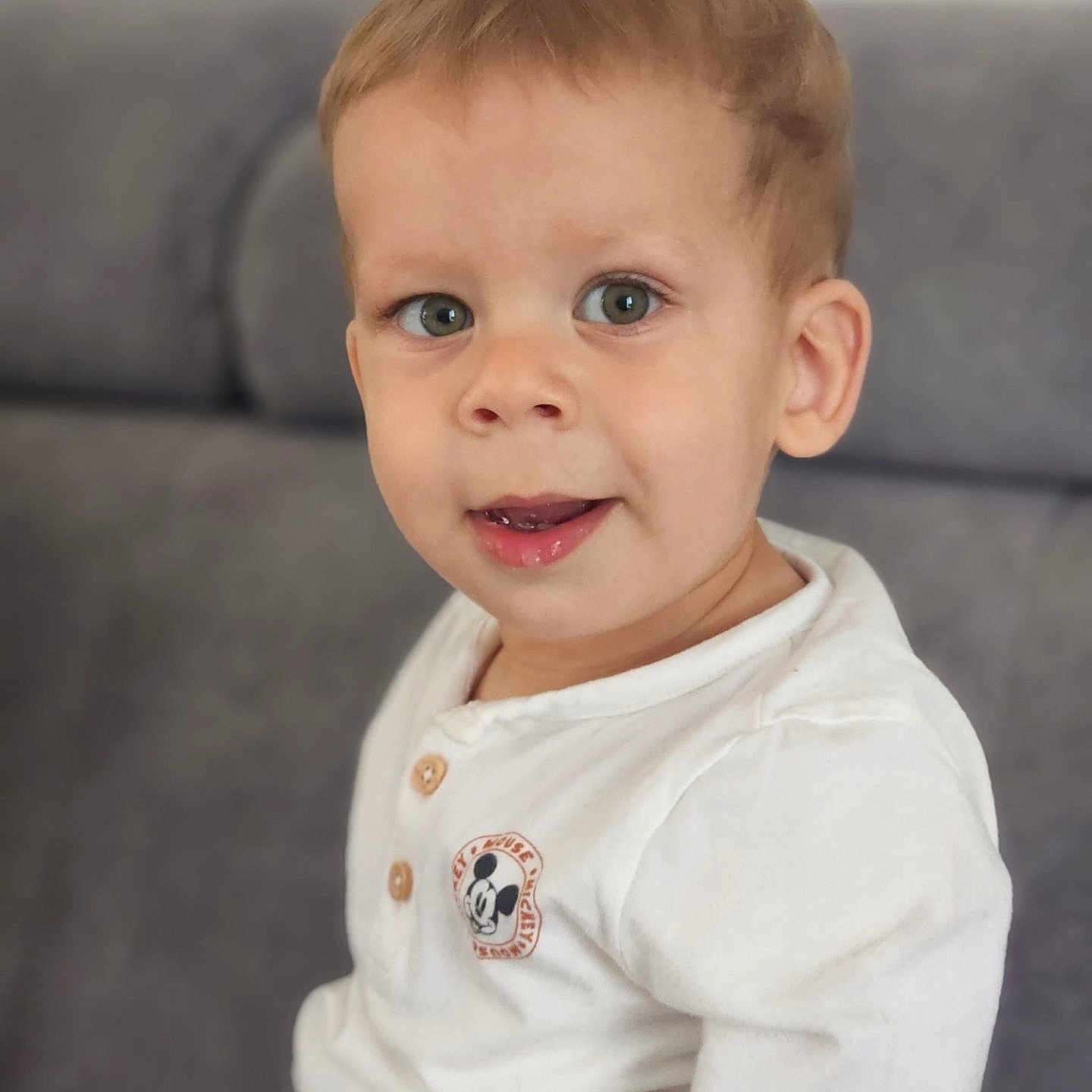 Noah participe au concours pour gagner de l'argent avec cette photo : baby, casual_clothing, child, couch, curious, cute, eyes, face, happy, head, indoor, light_brown_hair, mickey_mouse, person, portrait, seated, smile, toddler, white_shirt, young_child
