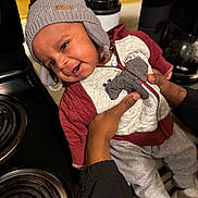 Jacobe joined the competition — help win amazing prizes! baby, child, hat, jacket, smile, kitchen, stove, coffee_maker, hand, person, clothing, infant, warm_clothes, cute, happy, indoors, cozy, face, socks, portrait