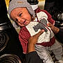 baby, child, hat, jacket, smile, kitchen, stove, coffee_maker, hand, person, clothing, infant, warm_clothes, cute, happy, indoors, cozy, face, socks, portrait
