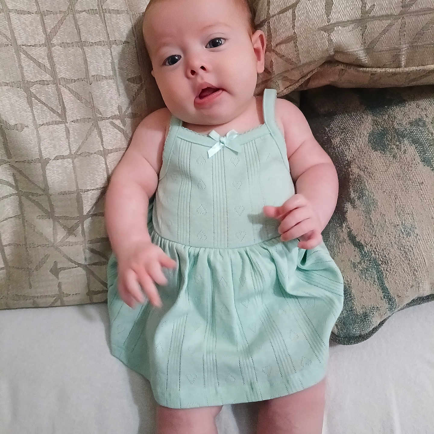 Trinity joined the competition — help win amazing prizes! baby, child, infant, mint_green_dress, couch, cushions, patterned, curious_expression, indoor, soft_lighting, portrait, chubby_cheeks, small_hands, seated, casual, closeup, skin, head, eyes, person