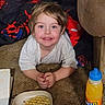 child, smiling, carpet, waffle, plate, orange_juice, bottle, blanket, couch, indoor, happy, messy_face, food, drink, young_child, person, casual_clothing, floor, lying_down, breakfast