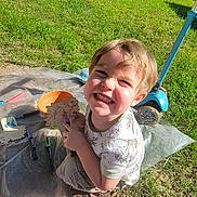 Ryder is registered to the contest to win money with this photo: child, smiling, outdoor, grass, scooter, wagon, craft, markers, sunlight, play, happy, toy, art, creative, summer, fun, person, wooden_craft, plastic_sheet, shoes