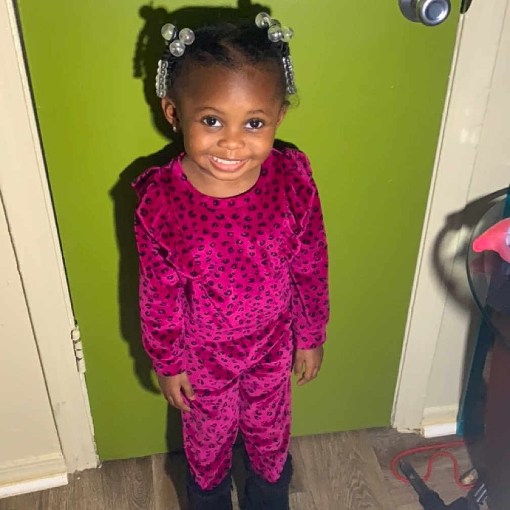 Aryana is registered to the contest to win money with this photo: accessories, child, clothing, coat, door, dress, face, female, footwear, formalwear, girl, head, lighting, pants, person, photography, portrait, purple, shoe, wood