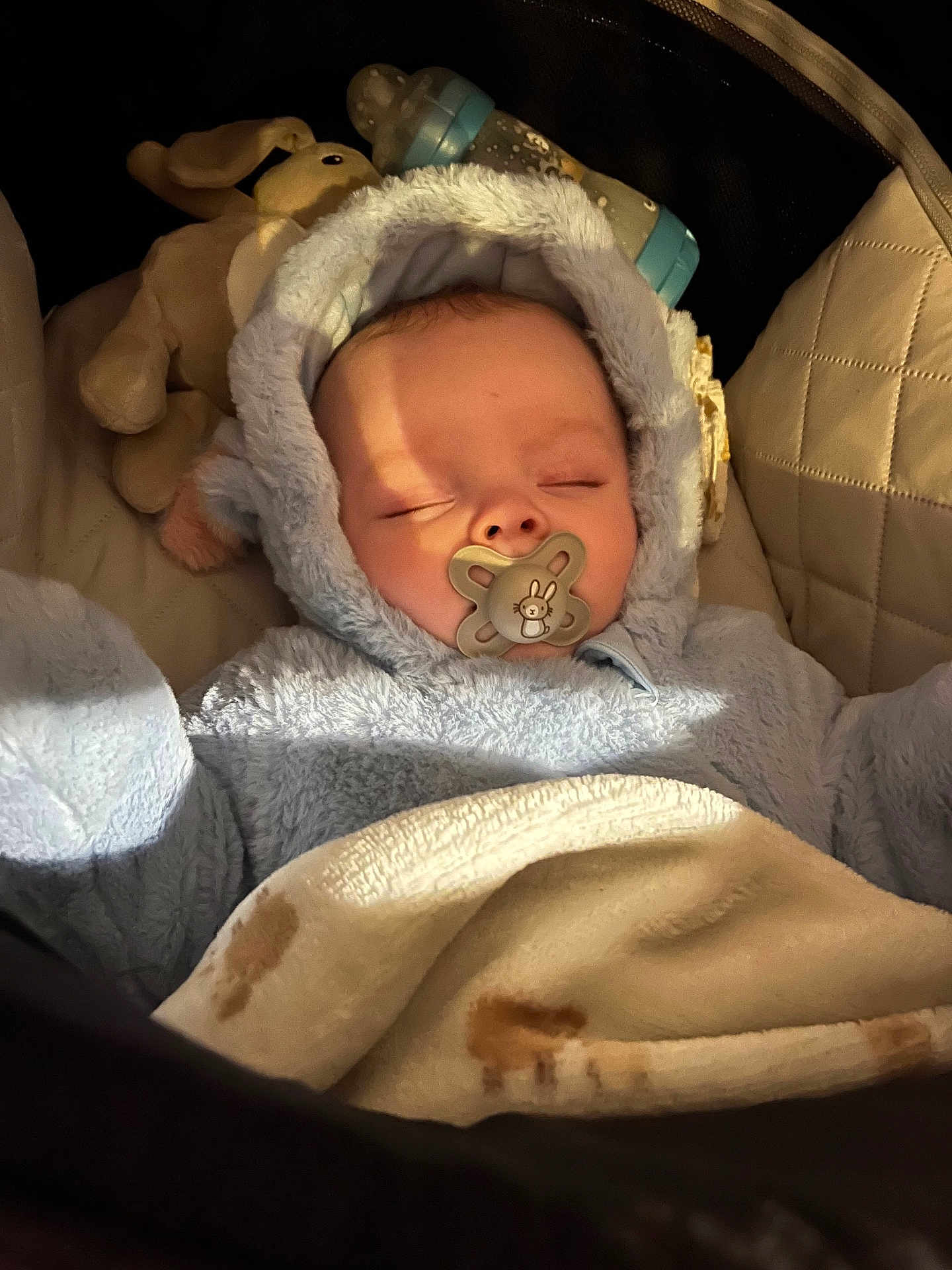 Arlo is registered to the contest to win money with this photo: baby, sleeping, pacifier, blue_outfit, blanket, plush_toy, baby_bottle, cozy, infant, close_up, cute, soft_lighting, indoor, child, face, headwear, warm, comfort, rest, peaceful
