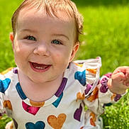 Oakley is registered to the contest to win money with this photo: baby, child, smiling, face, blue_eyes, teeth, grass, outdoor, sunlight, happy, heart_pattern, clothing, cute, portrait, infant, nature, skin, head, person, daylight