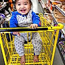 Miguel is registered to the contest to win money with this photo: baby, baby_clothing, barefoot, blue_jacket, bright_lighting, child, grocery_store, happy, indoor, laughing, onesie, portrait, retail, seasonal_decorations, shelves, shopping, shopping_cart, smiling, store_aisle, yellow_cart