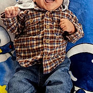 Miguel is registered to the contest to win money with this photo: baby, blanket, casual_clothing, child, close_up, colorful, face, happy, indoors, infant, jeans, joy, laughing, lying_down, plaid_shirt, playful, portrait, rocket, shoes, smiling