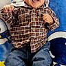 baby, child, infant, smiling, laughing, lying_down, portrait, face, happy, playful, plaid_shirt, jeans, shoes, blanket, rocket, colorful, indoors, close_up, casual_clothing, joy