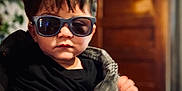 Josiah is registered to the contest to win money with this photo: toddler, child, sunglasses, black_shirt, denim_jacket, portrait, indoor, wooden_door, blurred_background, hair, fashion, person, cute, hand, face, casual, young_child, cool, expression, style