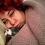 person, cat, blanket, curly_hair, red_hair, sleeping_cat, cozy, close_up, indoor, soft_lighting, resting, face, fur, whiskers, pillow, relaxing, intimate, warm, nap, comfort