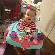 Kyoka is registered to the contest to win money with this photo: baby, child, walker, toy, red_bow, striped_shirt, indoor, floor, window, curtains, chair, carpet, wood_floor, smile, person, face, hands, feet, clothing, home