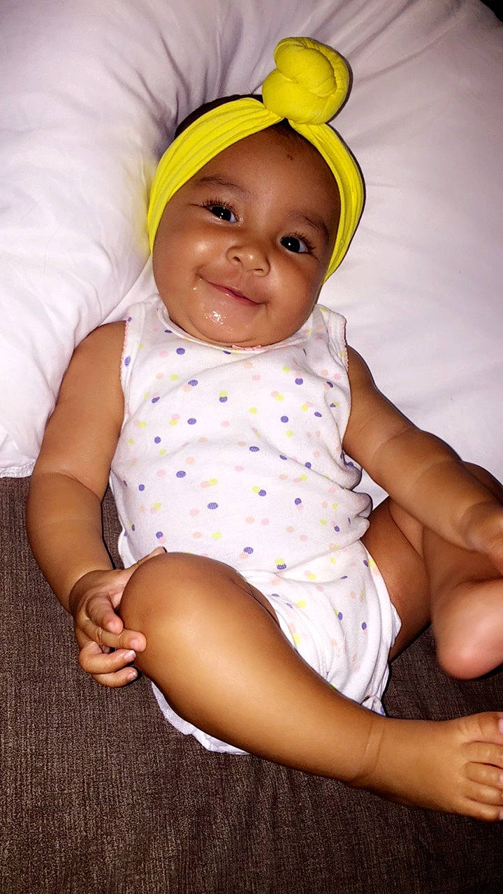 Avaiah is registered to the contest to win money with this photo: baby, baby_products, baby_toddler_clothing, child, happy, headgear, joy, person, product, sitting, skin, smile, toddler, yellow