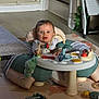 baby, infant, child, activity_center, play_mat, toy, plush_toy, seat, surprised_expression, blue_eyes, hands, floor, staircase, rug, living_room, indoor, furniture, playtime, clothing, portrait