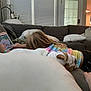 child, tablet, dog, bulldog, couch, pillows, living_room, indoor, casual, playing, relaxing, tie_dye_shirt, blonde_hair, furniture, technology, home, cozy, pet, sleeping, family