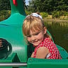 child, girl, smiling, outdoor, paddle_boat, boat, pond, water, nature, garden, trees, green, red_dress, floral_pattern, white_bow, blonde_hair, portrait, sunlight, recreation, summer