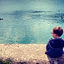 child, boy, glasses, pond, water, ducks, sitting, concrete, nature, outdoor, calm, reflection, grass, casual_clothing, blue, quiet, daylight, peaceful, solitude, young