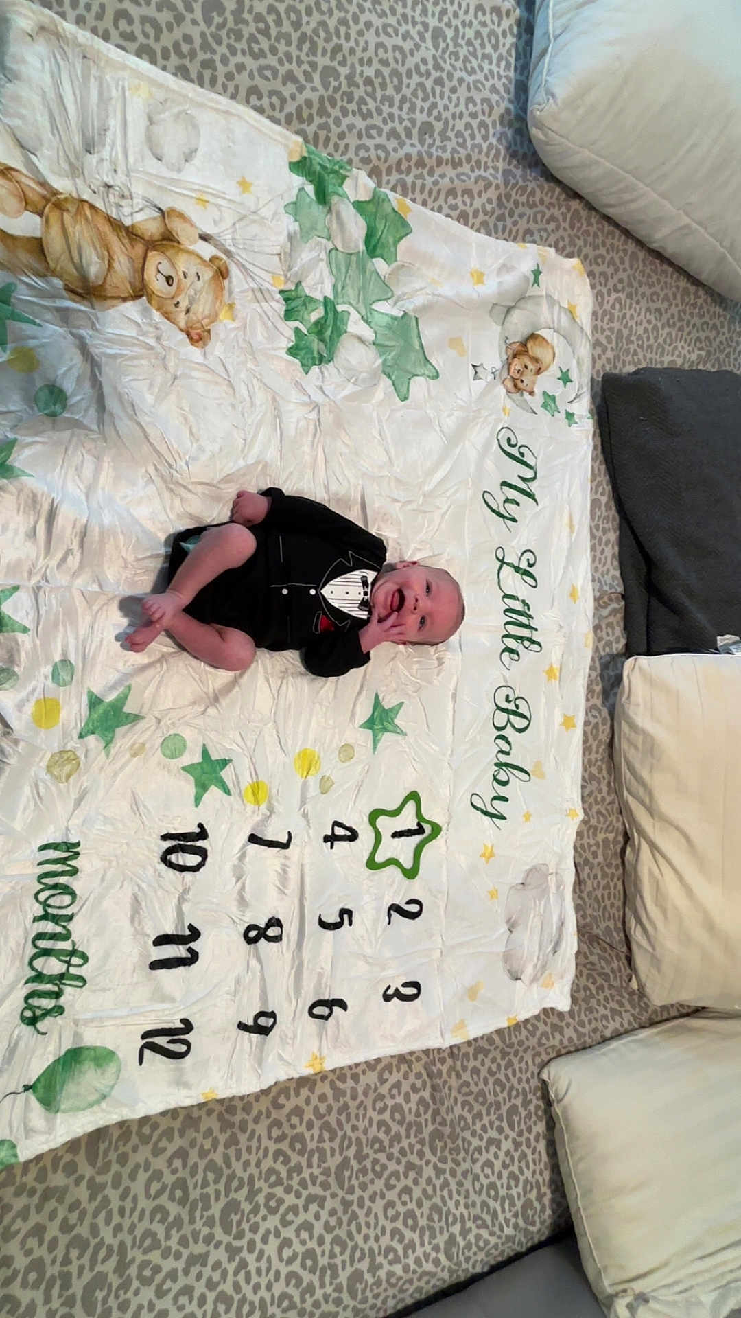 Ares joined the competition — help win amazing prizes! baby, infant, milestone_blanket, tuxedo_onesie, stars, teddy_bear, green, yellow, white, leopard_print, cushions, smiling, lying_down, indoors, baby_months, blanket, cute, child, one_month, decorative