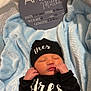 baby, newborn, sleeping, black_clothing, hat, blanket, blue_blanket, birth_announcement, sign, text, infant, person, cute, peaceful, soft_texture, indoors, portrait, resting, sleep, child