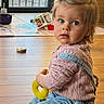 toddler, child, indoor, wooden_floor, toy, pink_sweater, blue_eyes, curly_hair, casual_clothing, sitting, playtime, daylight, home, window, flooring, denim_overalls, baby, cute, young_child, curious