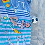 baby, beach, sand, striped_towel, dominoes, playing_cards, soccer_ball, toy_chicken, toy_rattle, toy_mirror, baby_clothes, outdoor, child, blue_stripes, white_stripes, footwear_absent, sunny, relaxation, playtime, summer